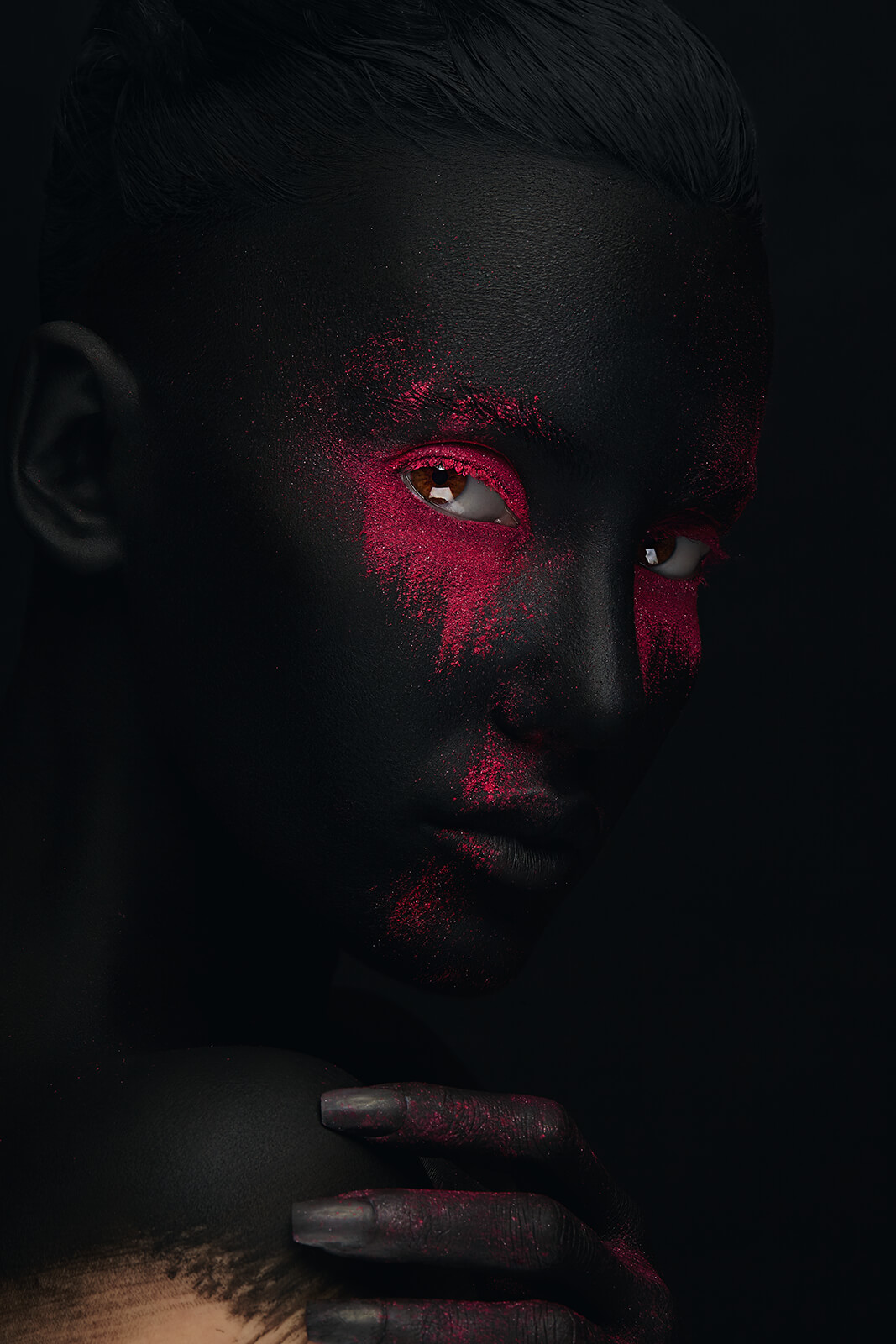 A creative headshot portrait with black makeup and red pigment accents.