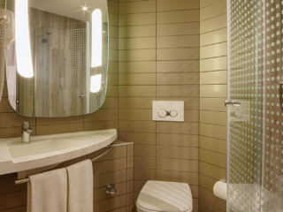 A contemporary bathroom at Ibis Hotel Tuzla with warm lighting, a glass shower, and elegant design.
