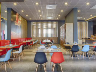 Interior view of the Ibis Hotel Tuzla restaurant featuring colorful modern chairs, a stylish buffet, and warm lighting for an inviting dining experience.