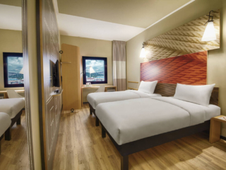 A stylish twin room at Ibis Hotel Tuzla, showcasing two comfortable beds, wooden floors, and a modern interior design.