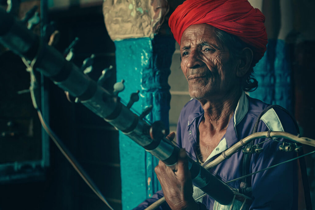 Close-up of an Indian folk musician in a red turban, playing a Ravanahatha instrument.