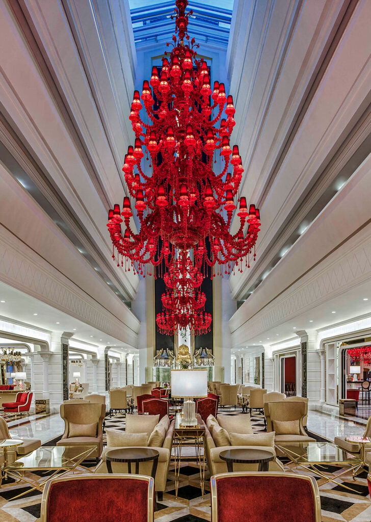 Luxurious lobby of Kaya Artemis Resort in Cyprus featuring a grand red chandelier and elegant seating.