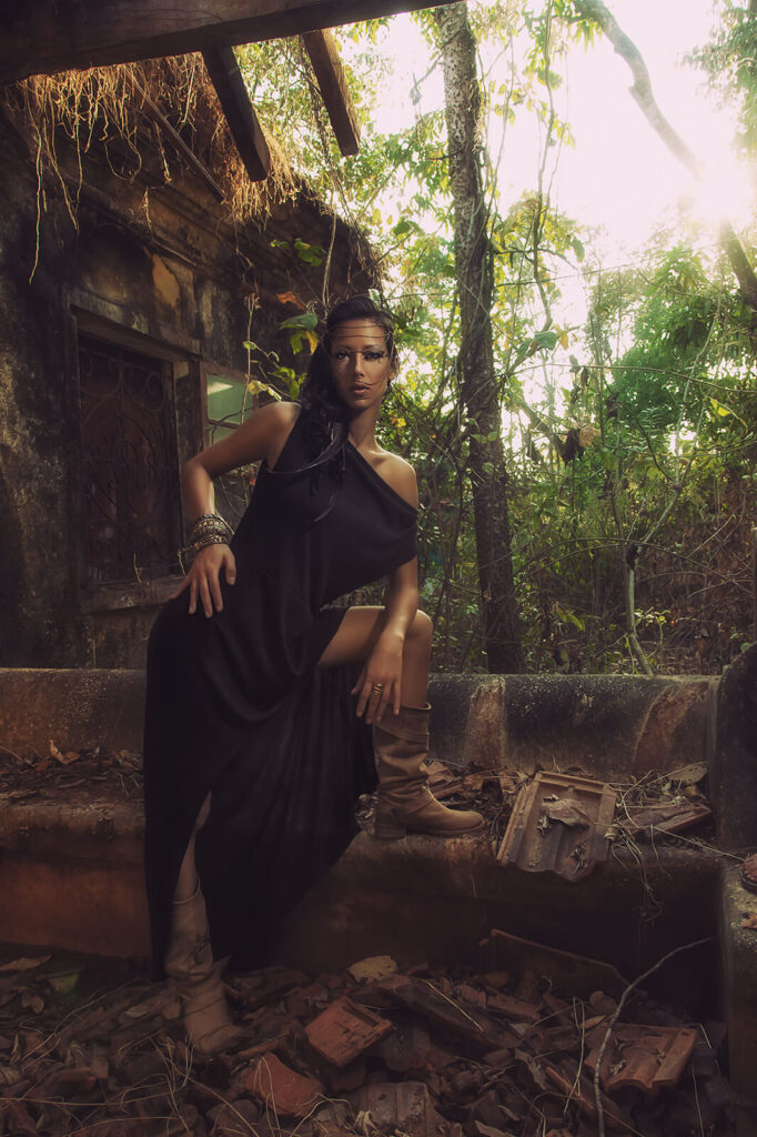 A mystical queen in a dark gown poses in an overgrown ruin, illuminated by golden sunlight.