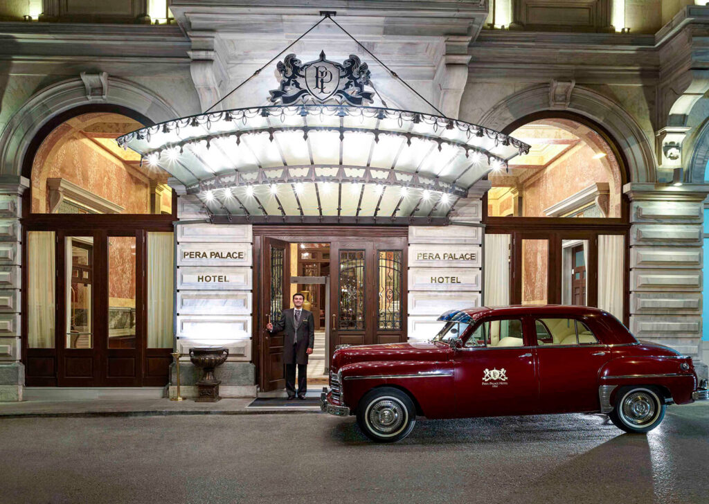 Historic entrance of Pera Palace Hotel in Istanbul with a vintage car parked in front.