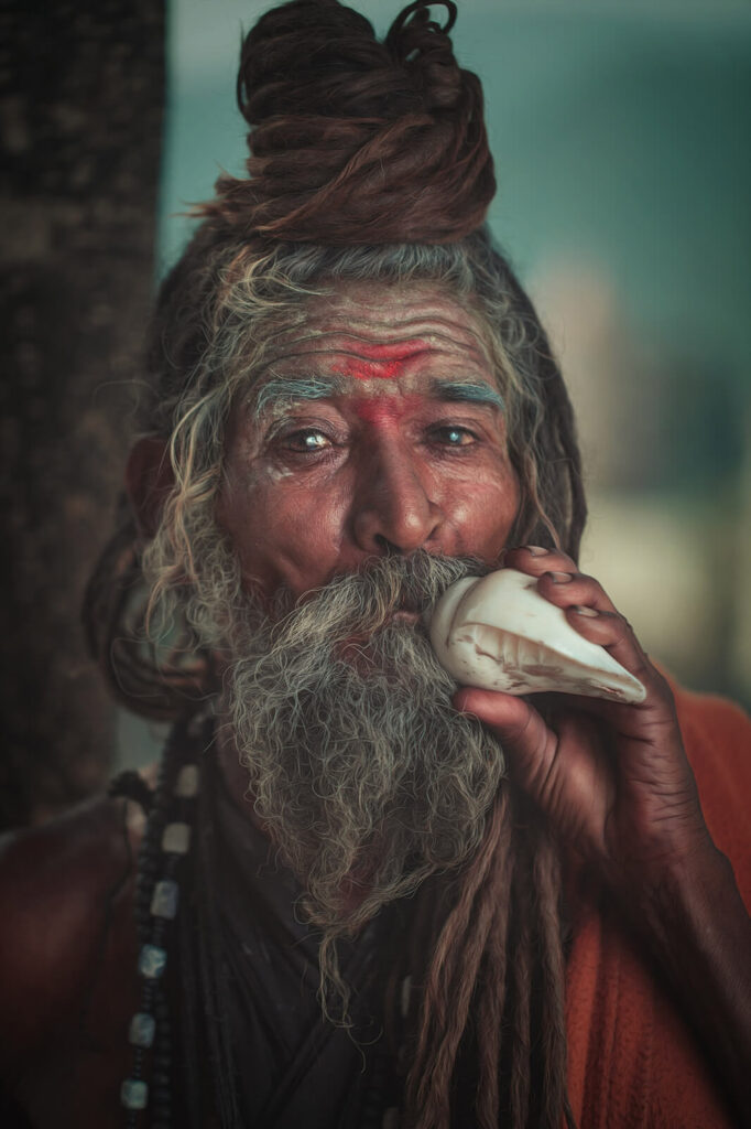 A Sadhu with long dreadlocks and sacred markings blowing a white conch shell.