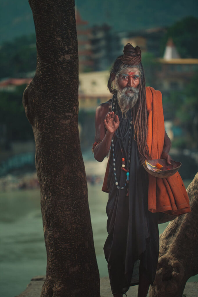 An Indian Sadhu with long dreadlocks, wearing an orange shawl, standing by the Ganges River.